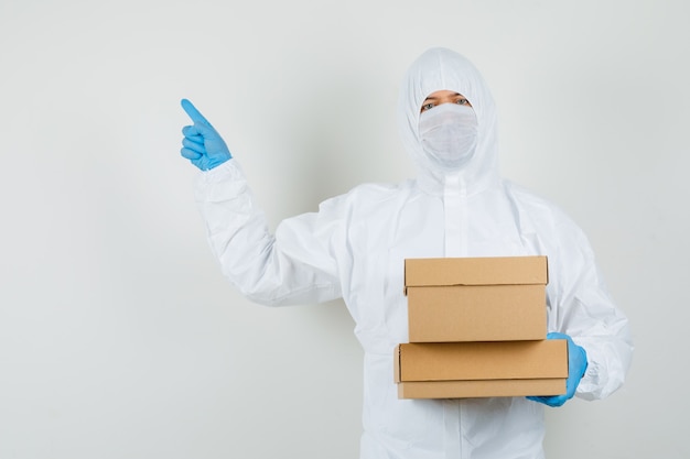 Male doctor pointing away while holding cardboard boxes in protective suit