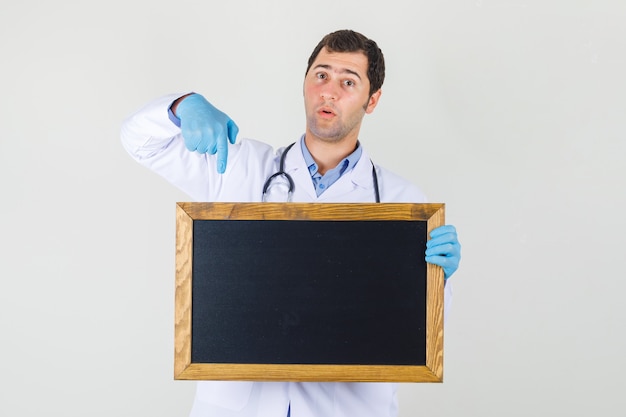 Мужчина-врач указывая пальцем на доску в белом халате, перчатки