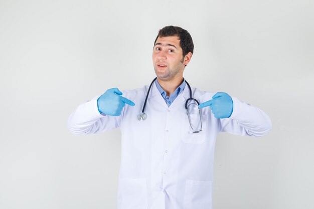 흰색 코트, 장갑에 자신의 손가락을 가리키고 자랑스럽게 찾고 남성 의사. 전면보기.