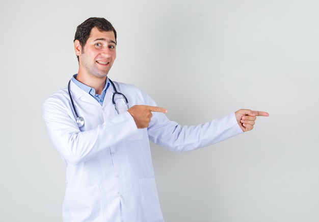 Male doctor pointing fingers to side in white coat and looking cheerful