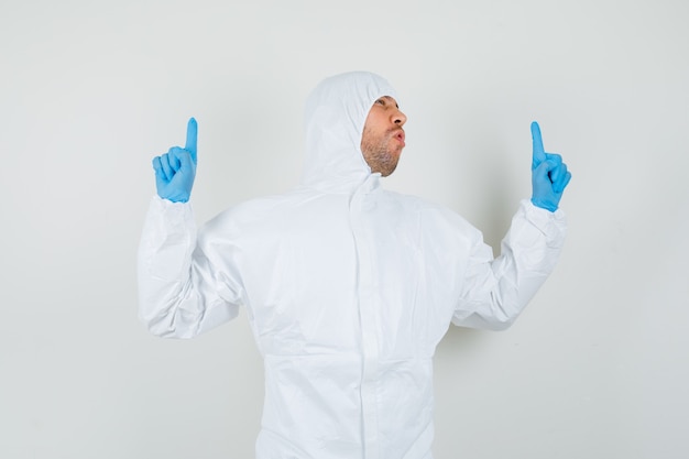 Male doctor pointing up in protective suit, gloves and looking lucky.