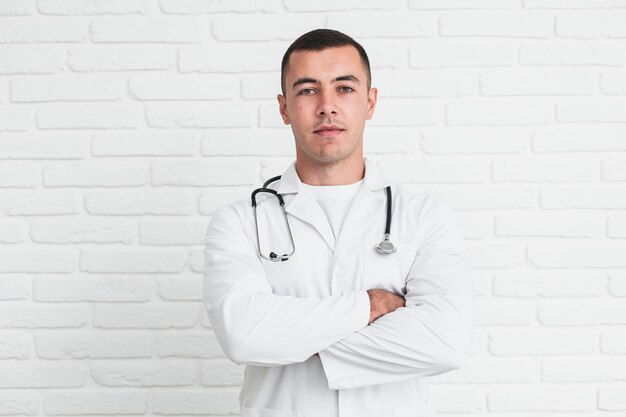 Male doctor posing in front of white bricks wall