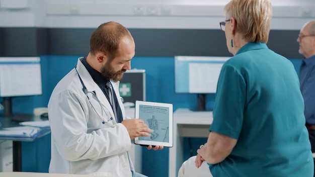 Free photo male doctor showing human skeleton illustration on digital tablet to senior woman at checkup examination. physician and patient looking at osteopathy diagnosis with bones and spinal cord.