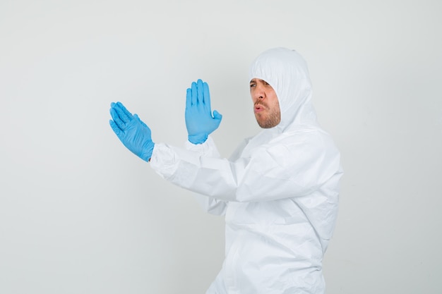 Male doctor showing karate chop gesture in protective suit, gloves and looking powerful