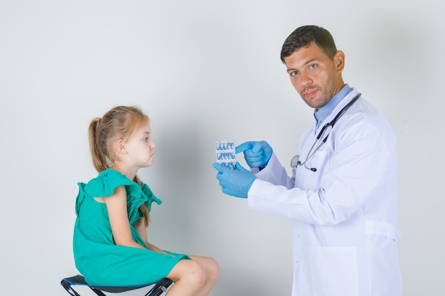 Male doctor showing pills while child sitting exhausted in white uniform front view.