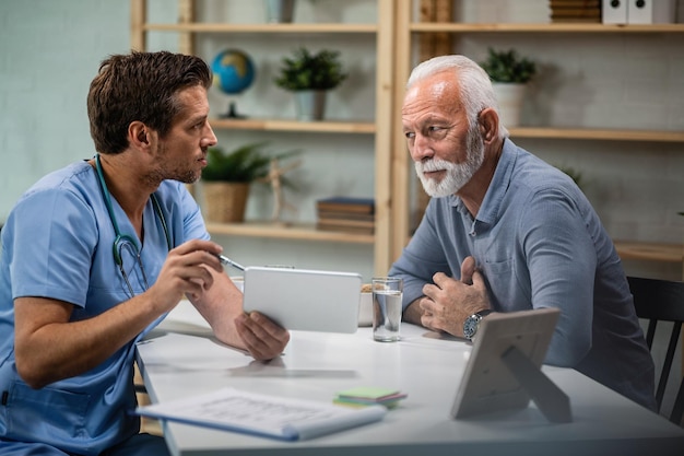 Male doctor using touchpad and explaining medical test results to his senior patient during medical appointment