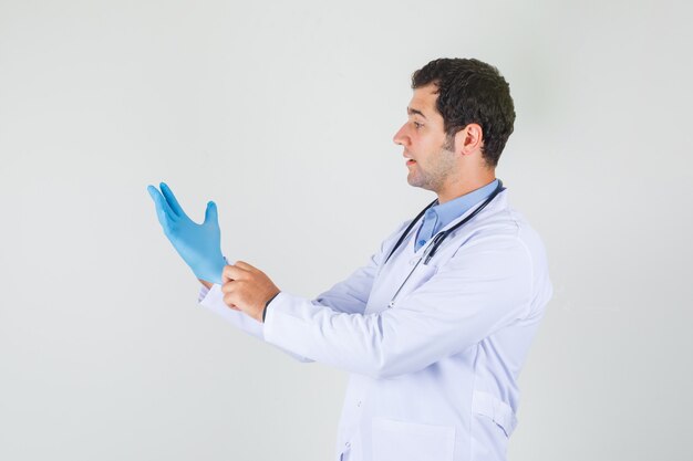 Male doctor wearing blue medical gloves in white coat and looking careful. .