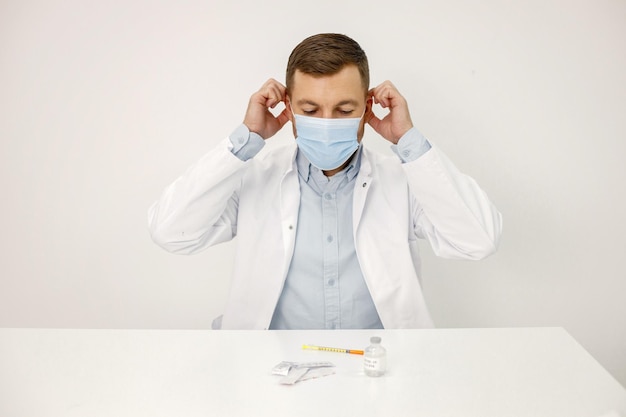 Foto gratuita medico maschio che indossa una maschera facciale mentre è seduto isolato su sfondo bianco