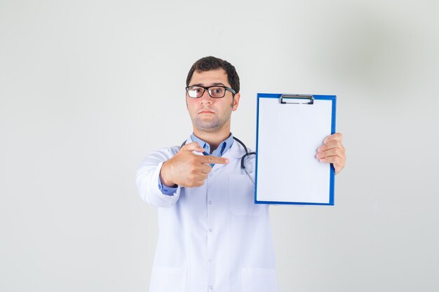 Male doctor in white coat, glasses pointing finger at clipboard and looking serious