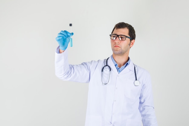 Male doctor in white coat, gloves, glasses holding test tube and looking serious