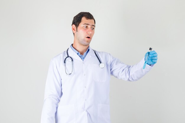 Male doctor in white coat, gloves holding test tube and looking surprised