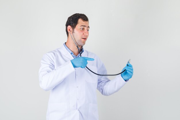 Male doctor in white coat, gloves pointing finger at stethoscope