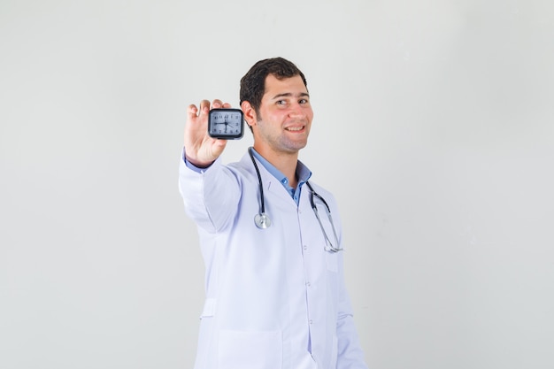 Male doctor in white coat holding clock and looking cheery