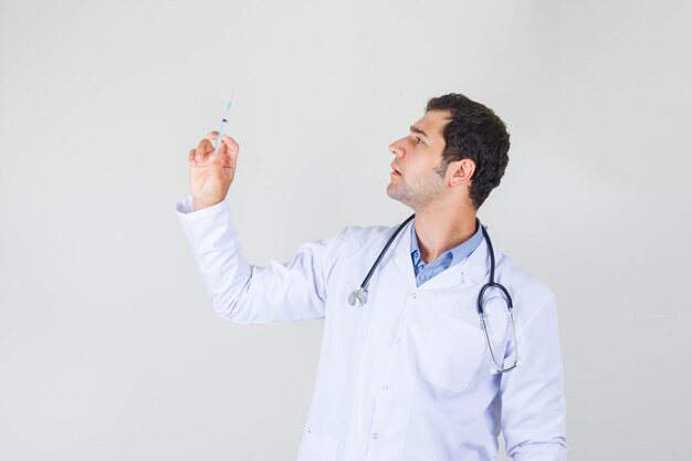 Male doctor in white coat holding syringe for injection and looking serious .