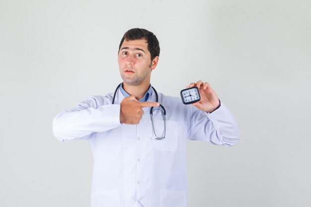 Male doctor in white coat pointing finger at clock and looking careful