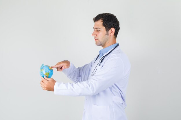 Male doctor in white coat putting finger on globe .