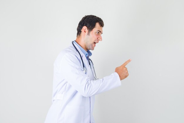 Male doctor in white coat, shouting and warning somebody and looking nervous .