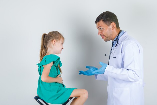Male doctor in white coat trying to identify trouble with child and looking careful