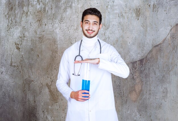 Male doctor with stethoscope holding a chemical flask with blue liquid inside.