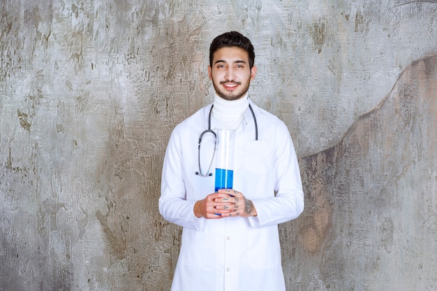 파란색 액체가 들어 있는 화학 플라스크를 들고 있는 청진기를 가진 남성 의사