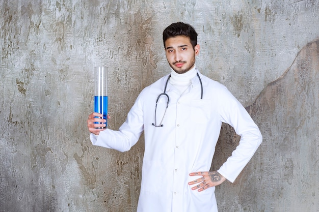中に青い液体が入った化学フラスコを保持している聴診器を持つ男性医師
