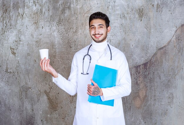 Male doctor with stethoscope holding a cup and a blue folder