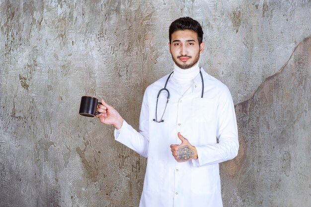Мужчина-врач со стетоскопом держит чашку кофе и наслаждается вкусом