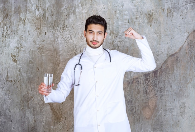 Male doctor with stethoscope holding a glass of pure water and showing positive hand sign