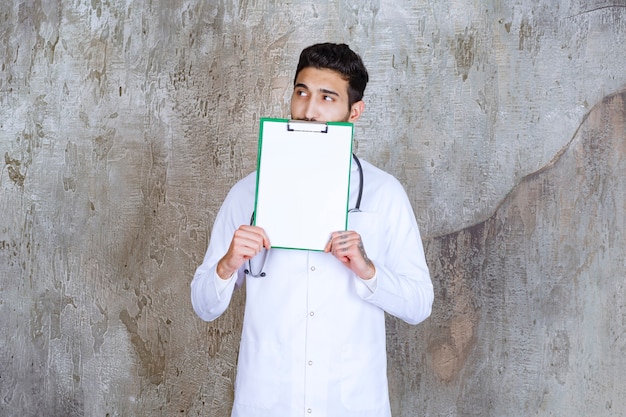 Male doctor with stethoscope holding the history of the patient and looks thoughtful.