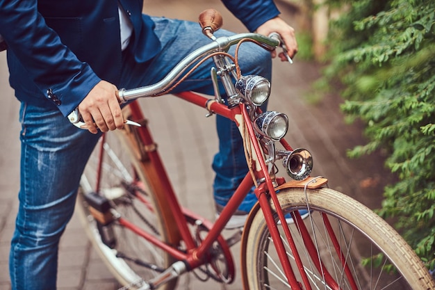 Male dressed in casual clothes, sitting on a retro bicycle in a city park.