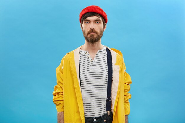 male dressed in stylish headwear and cloak posing at blank blue studio wall