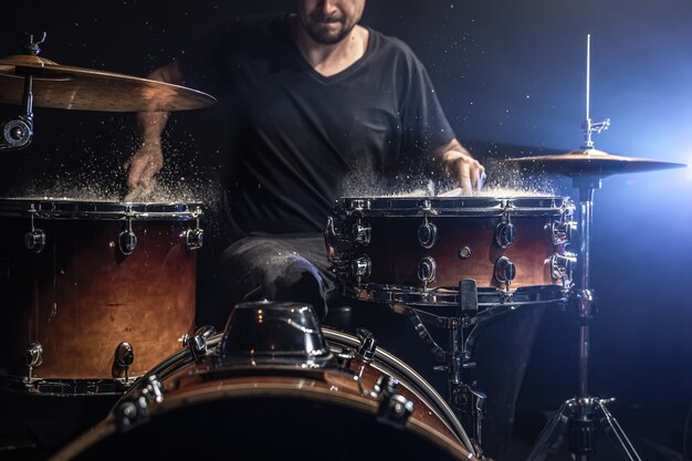 A male drummer plays drum sticks on a snare drum with splashing water in a dark room.