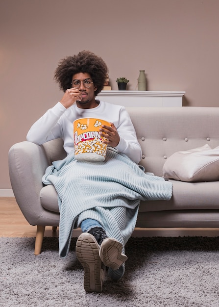 Мужчина ест попкорн на диване
