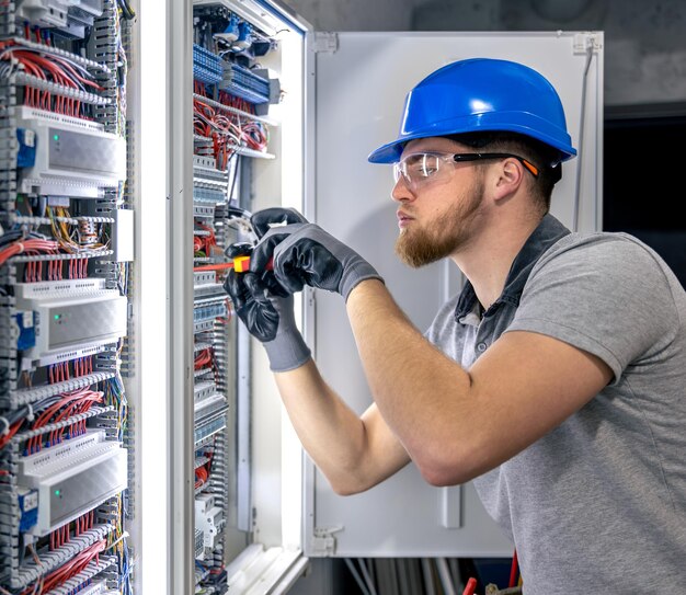 ユニフォームを着た男性電気技師がスイッチボードで働いています