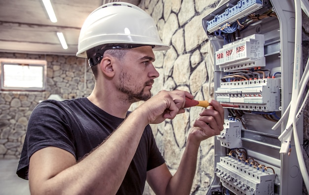 男性の電気技師は、電気接続ケーブルを使用して配電盤で作業します