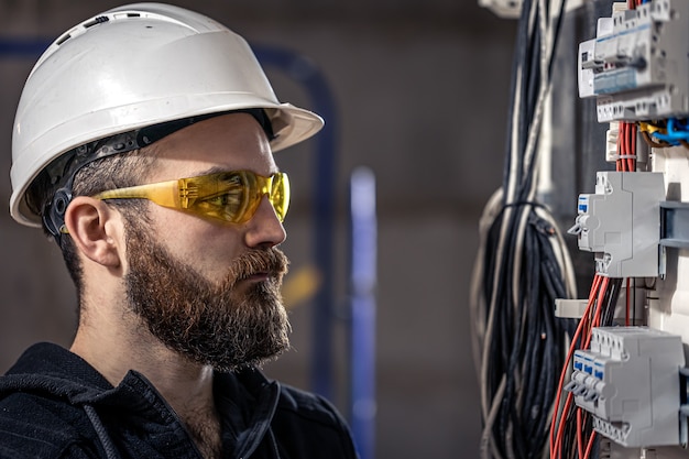 A male electrician works in a switchboard with an electrical connecting cable