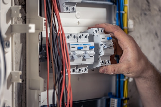 A male electrician works in a switchboard with an electrical connecting cable