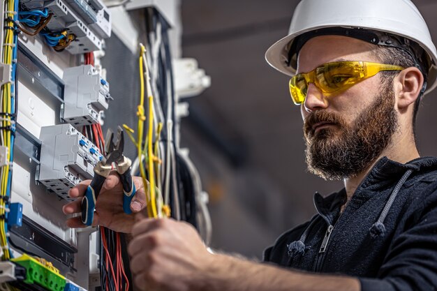 男性の電気技師は、電気接続ケーブルを使用して配電盤で作業します。