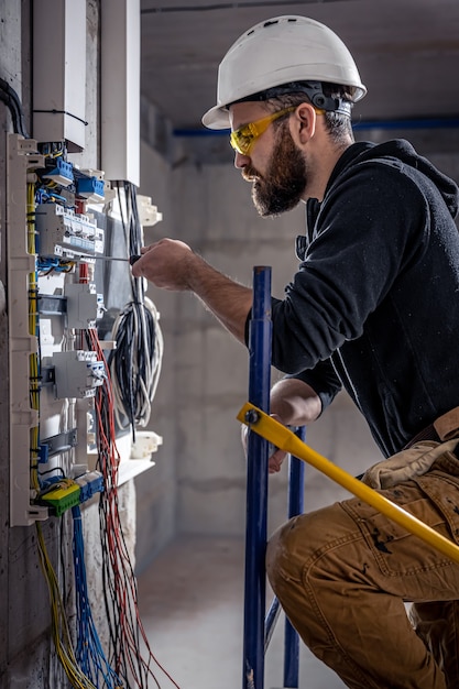 男性の電気技師は、電気接続ケーブルを使用して配電盤で作業します。