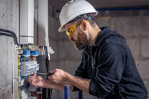 A male electrician works in a switchboard with an electrical connecting cable. Premium Photo