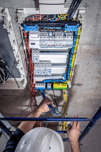 A male electrician works in a switchboard with an electrical connecting cable.