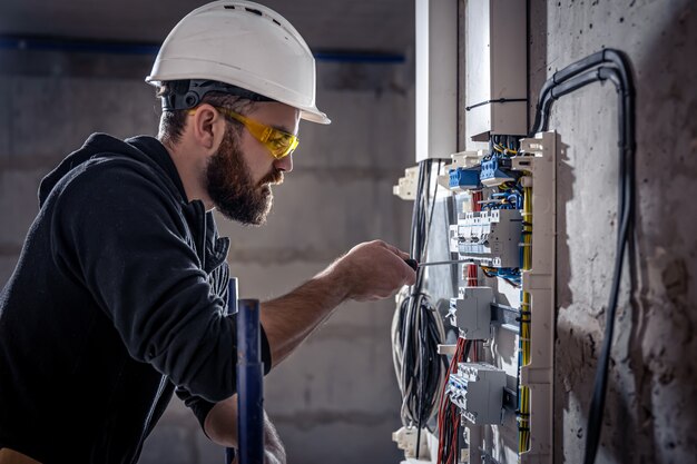 男性の電気技師は、電気接続ケーブルを使用して配電盤で作業します。