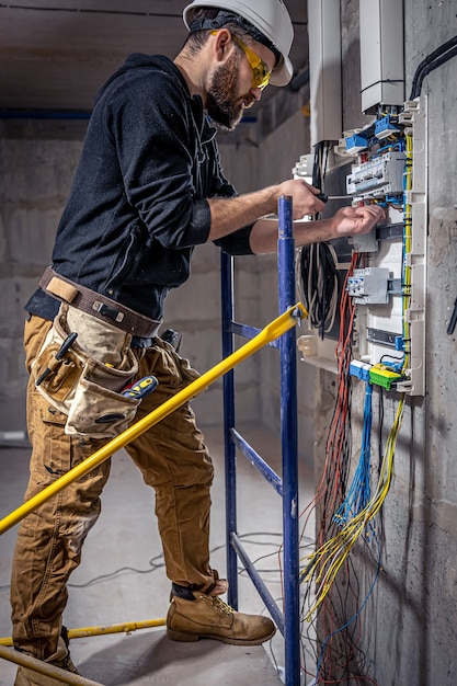 A male electrician works in a switchboard with an electrical connecting cable.