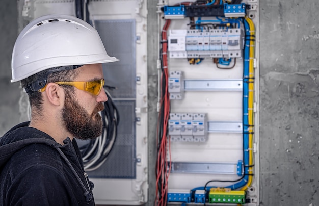 男性の電気技師は、電気接続ケーブルを使用して配電盤で作業します