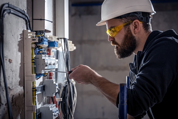 A male electrician works in a switchboard with an electrical connecting cable