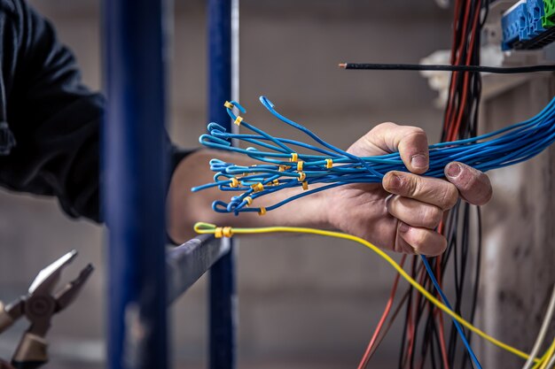 A male electrician works in a switchboard with an electrical connecting cable