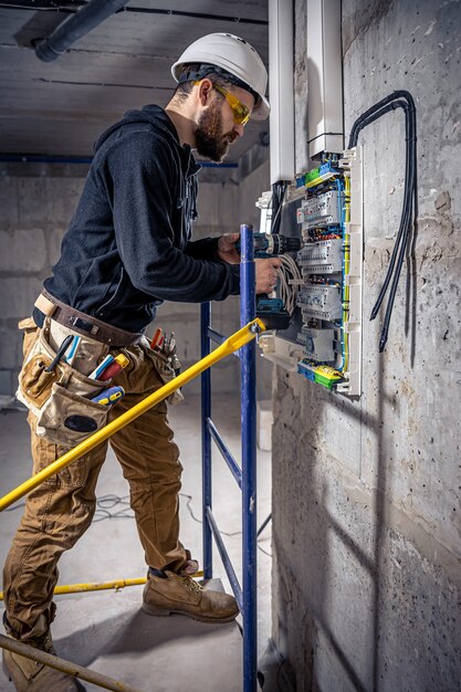 男性の電気技師は、電気接続ケーブルを使用して配電盤で作業します