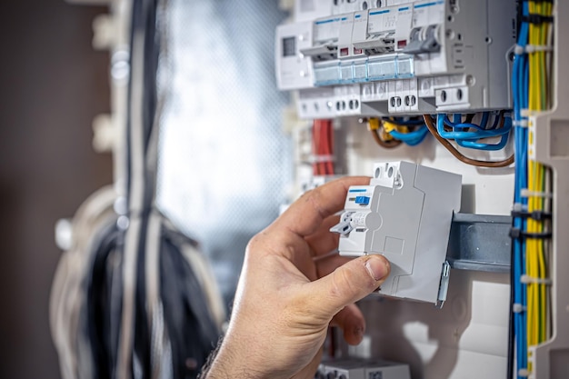 A male electrician works in a switchboard with an electrical connecting cable