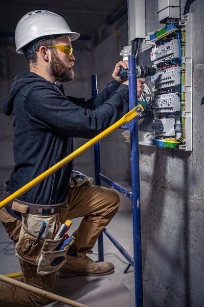 A male electrician works in a switchboard with an electrical connecting cable