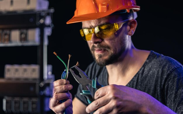 A male electrician works in a switchboard with an electrical connecting cable